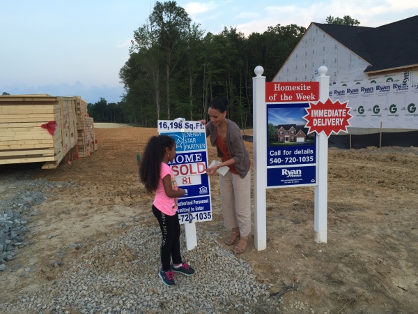 Relocation clients are shown here placing a sold sticker on a home site sign of Ryan Homes at Liberty Knolls in Stafford County.